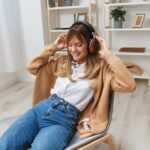 cheerful-young-blonde-lady-warm-sweater-headphones-listen-enjoy-fav-songs-dancing-sitting-armchair-modern-home-interior-music-time-relaxing-cool-playlist-concept-copy-space_163305-262782
